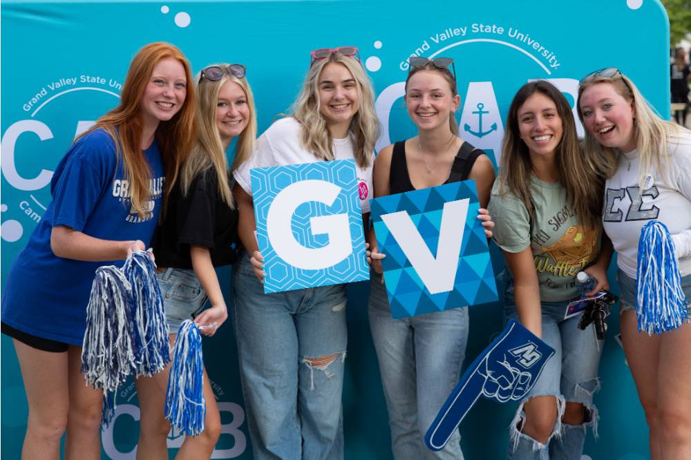 six students posing in front of CAB backdrop at Laker Kickoff photo booth and holding GV letters